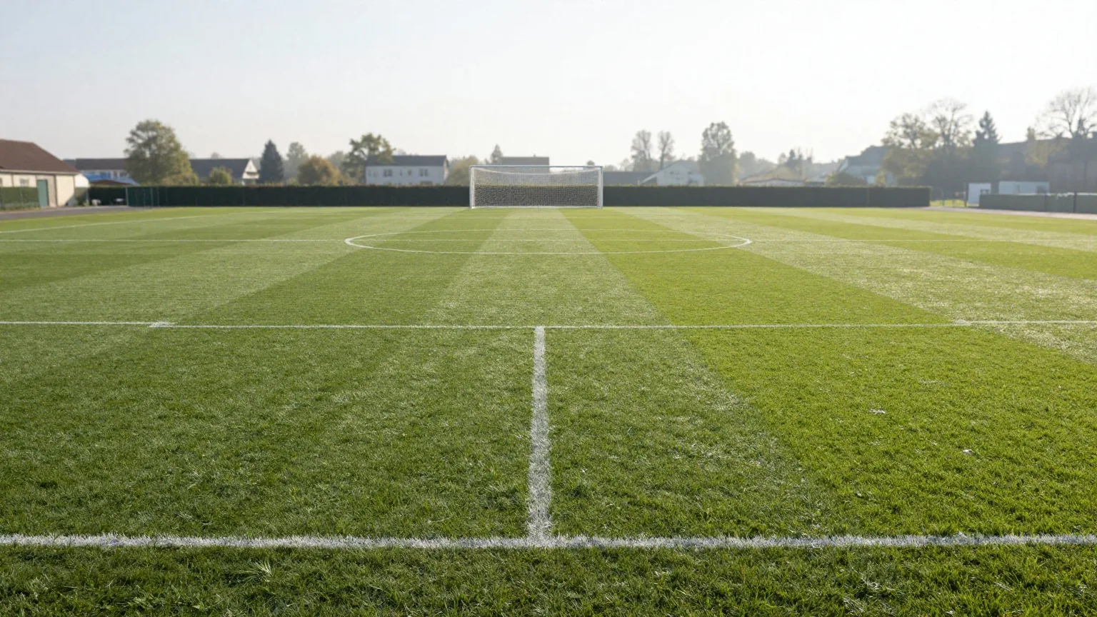 Leeres Fußballfeld im Morgenlicht mit frisch gezogenen weißen Linien, Mittelkreis und Tor im Hintergrund