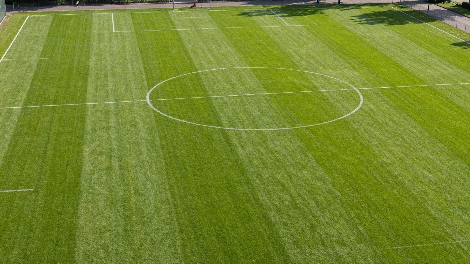 Luftaufnahme eines leeren Fußballfelds mit weißen Linien, Mittelkreis und beiden Strafräumen auf gestreiftem Rasen