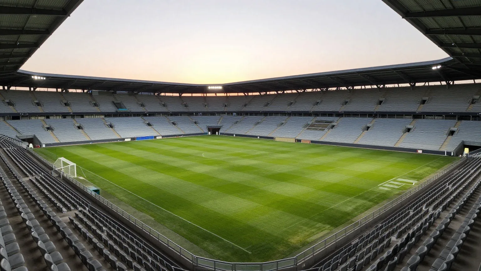 Leeres Fußballstadion im Abendlicht von der oberen Tribüne aus, Flutlicht an, Rasen mit Mähstreifen