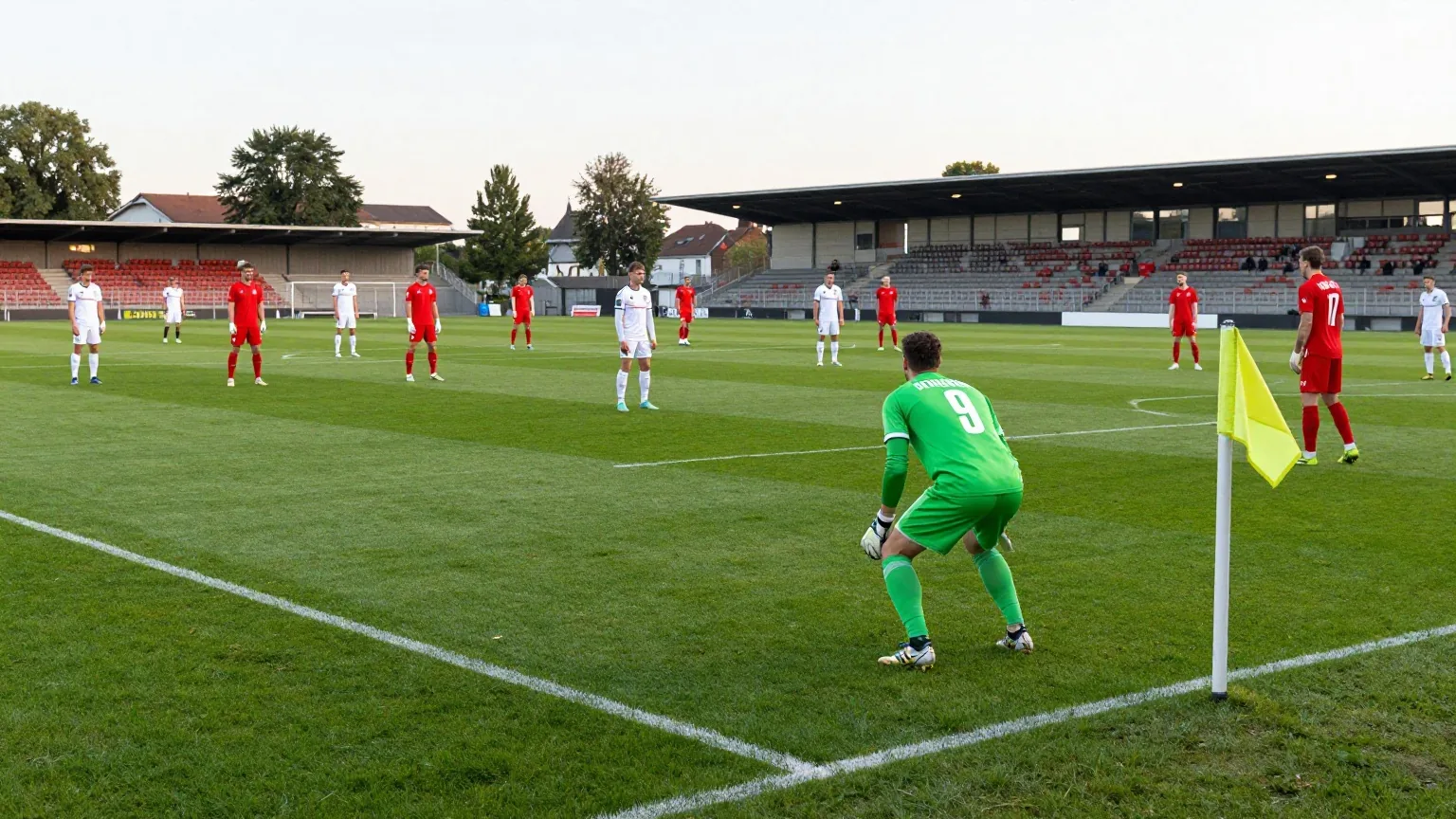 Spieler in roten und weißen Trikots verteilen sich über das Spielfeld, vorn steht ein Torhüter in Grün
