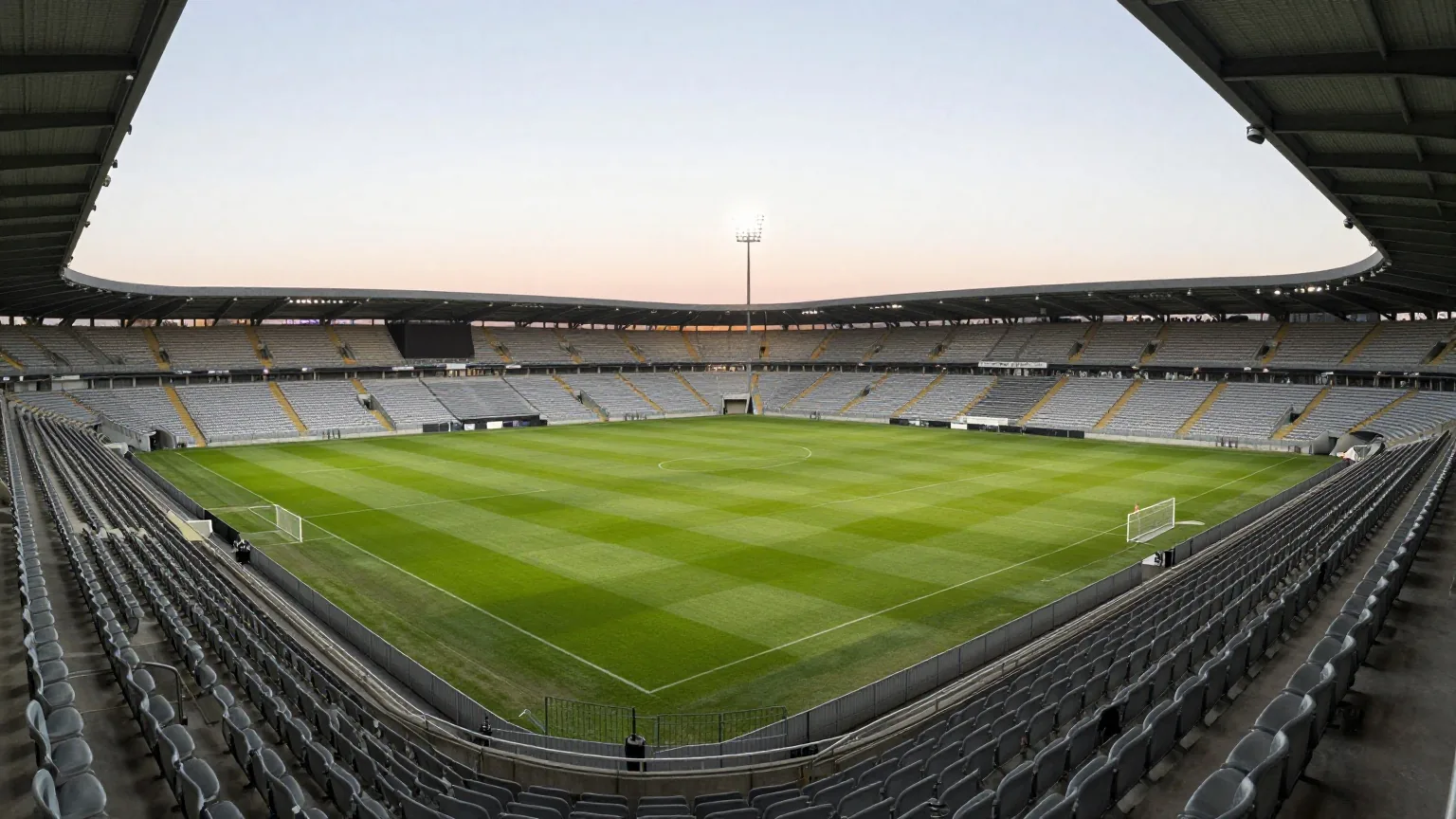 Leeres Fußballstadion bei Sonnenuntergang von der oberen Tribüne aus, Flutlicht an, Rasen mit Mähstreifen