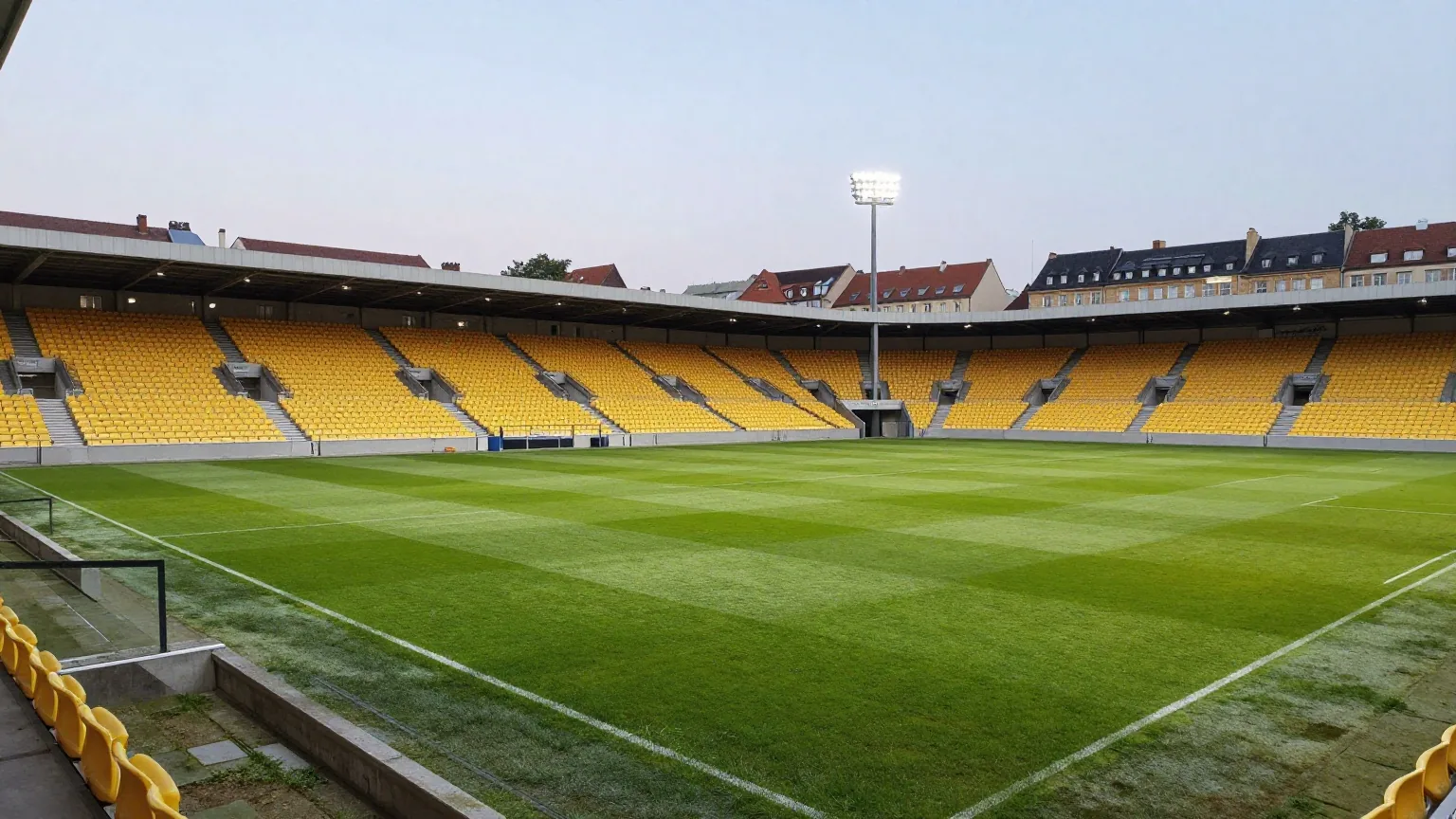Modernes Fußballstadion mit gelben Sitzen am Rand einer historischen Stadt in der Abenddämmerung mit eingeschaltetem Flutlicht