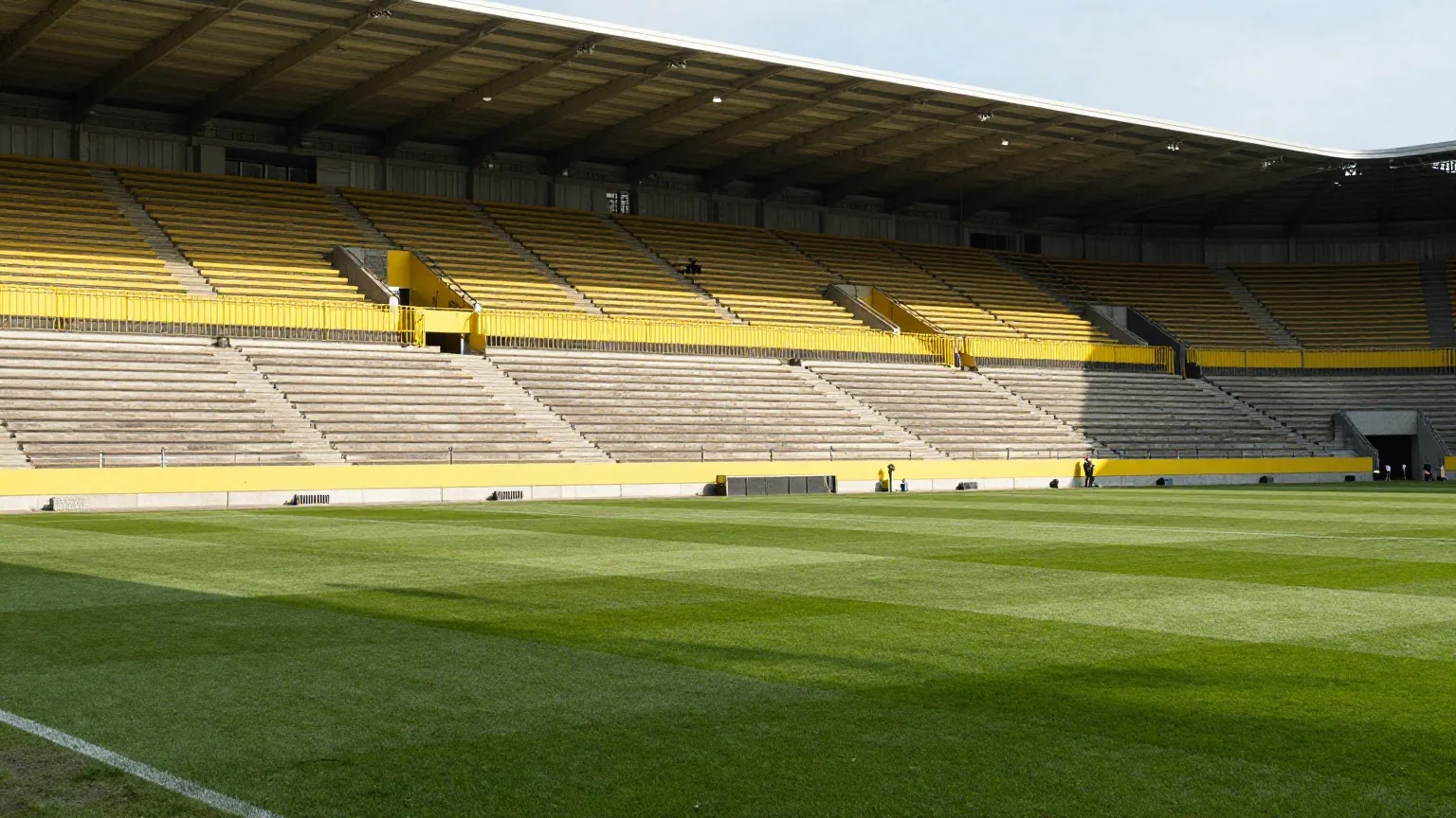 Riesige steile Stehtribüne in einem leeren Stadion mit gelben Wellenbrechern im Licht des späten Nachmittags