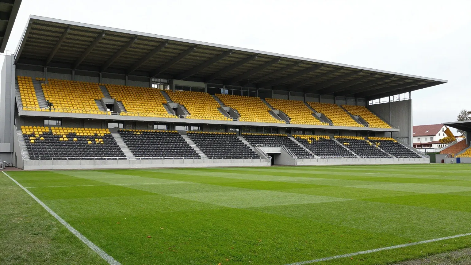 Modernes Fußballstadion mit durchgehendem Dach und gelb-schwarzen Sitzen an einem klaren Herbstnachmittag