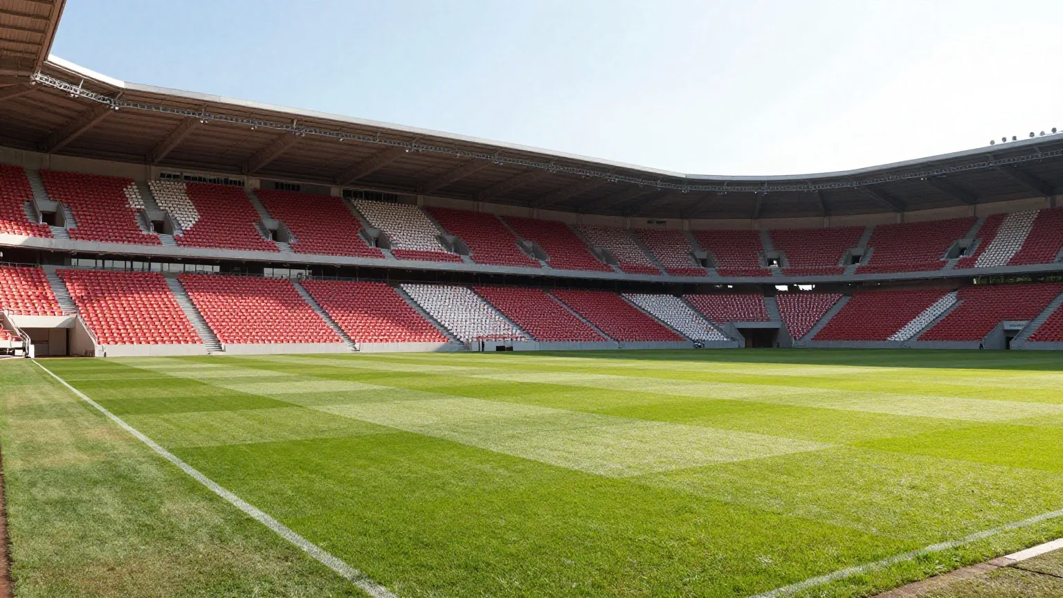 Mittelgroßes Fußballstadion mit rot-weißen Sitzen und steiler Stehtribüne im warmen Abendlicht