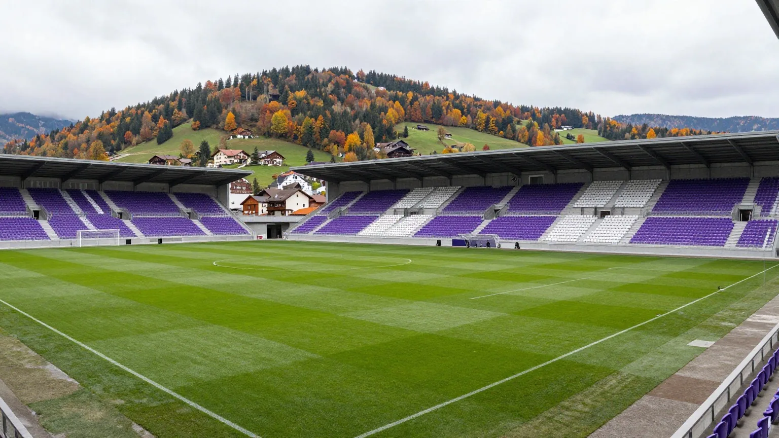 Kompaktes modernes Fußballstadion mit lila-weißen Sitzen an einem bewaldeten Hang im Herbst