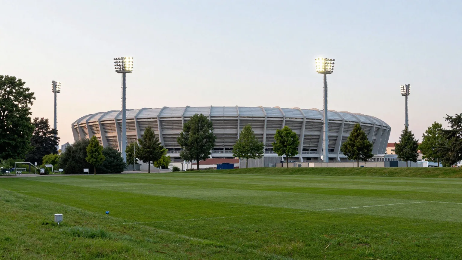 Großes Fußballstadion in einem Park in der Abenddämmerung, vier Ecktürme mit eingeschalteten Flutlichtern