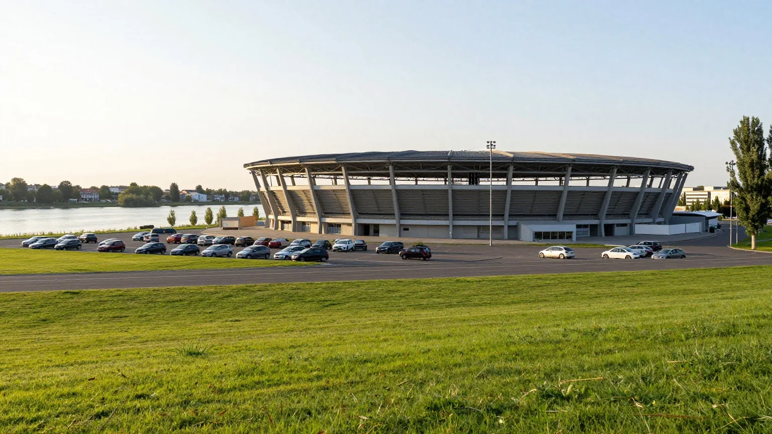 Kompaktes modernes Fußballstadion mit dunklem Dach in einer Flusslandschaft im Abendlicht
