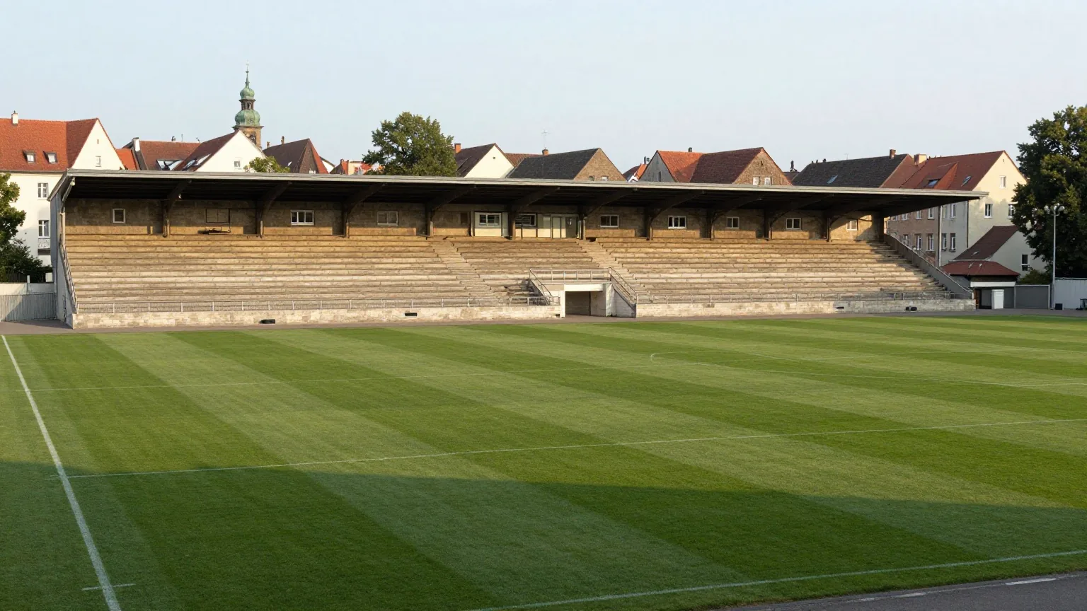 Traditionelles Fußballstadion mit langer überdachter Haupttribüne aus Stein und offenen Stehrängen im Abendlicht