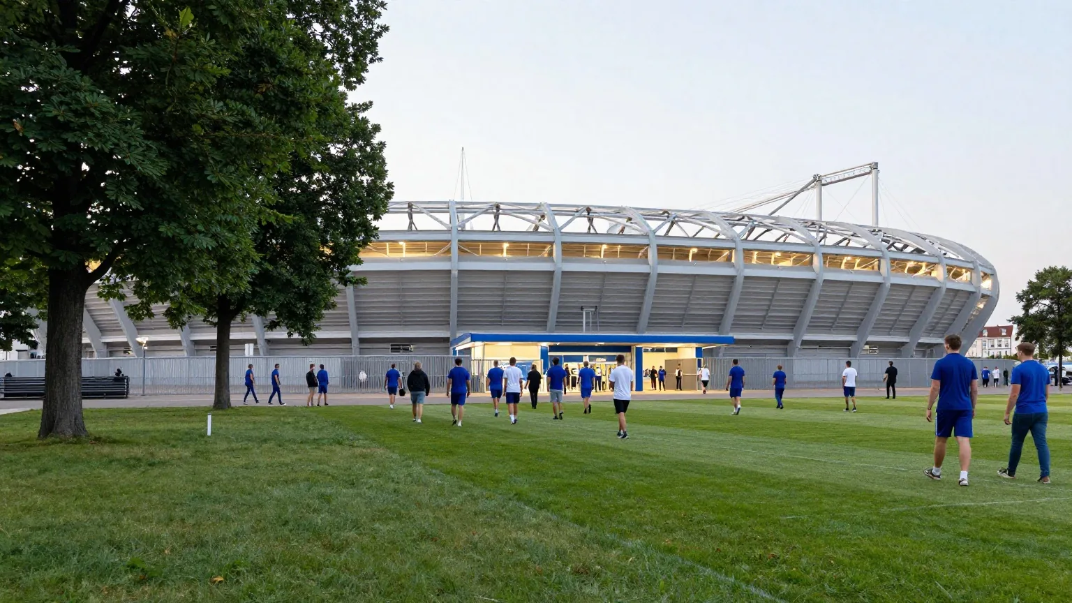 Großes Fußballstadion in einem Park in der Abenddämmerung, Besucher gehen in blauer und weißer Kleidung zu den Eingängen