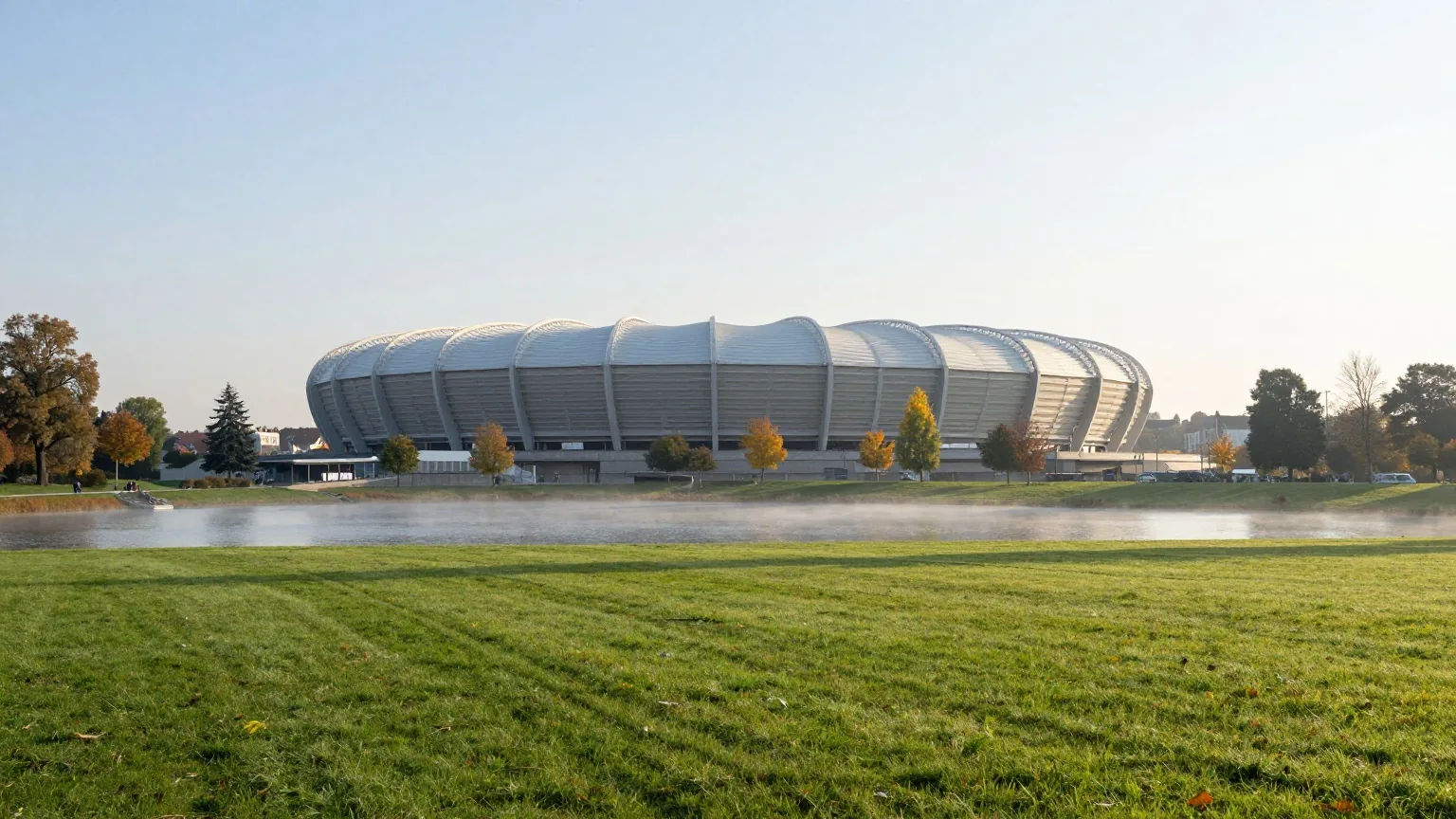 Großes modernes Fußballstadion mit wellenförmigem Dach an einem See und Park im herbstlichen Morgennebel
