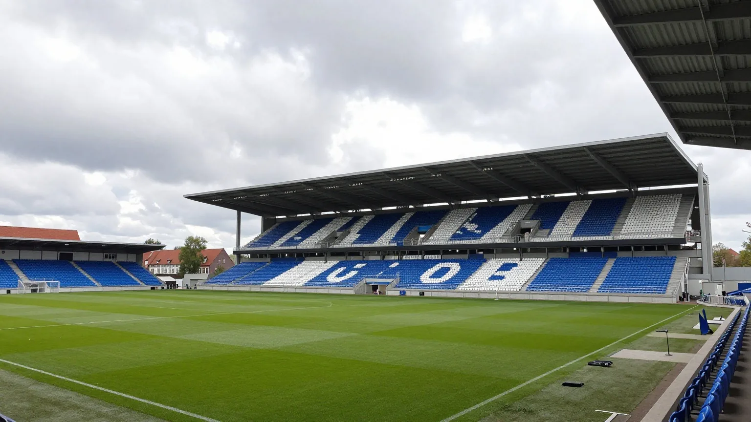 Kompaktes Fußballstadion mit steilen überdachten Tribünen an einem windigen Tag mit Wolken und Sonnenlücken