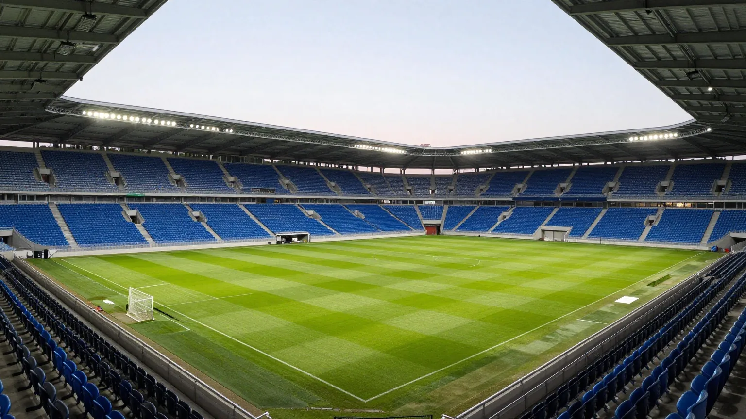 Kompaktes modernes Fußballstadion mit blauen und schwarzen Sitzen in der Abenddämmerung bei eingeschaltetem Flutlicht