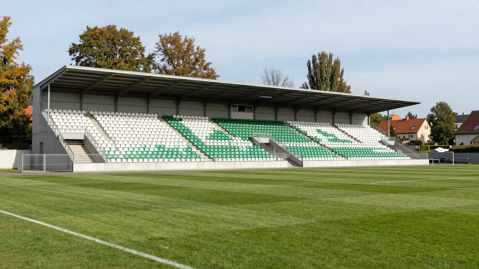 Traditionsreiches Fußballstadion mit überdachten Tribünen, weißen und grünen Sitzen und alten Bäumen im Herbstlicht