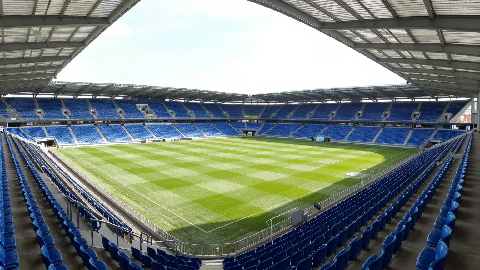 Kompaktes Fußballstadion mit steilen blauen Sitzreihen unter einem Dach an einem hellen Frühlingsnachmittag