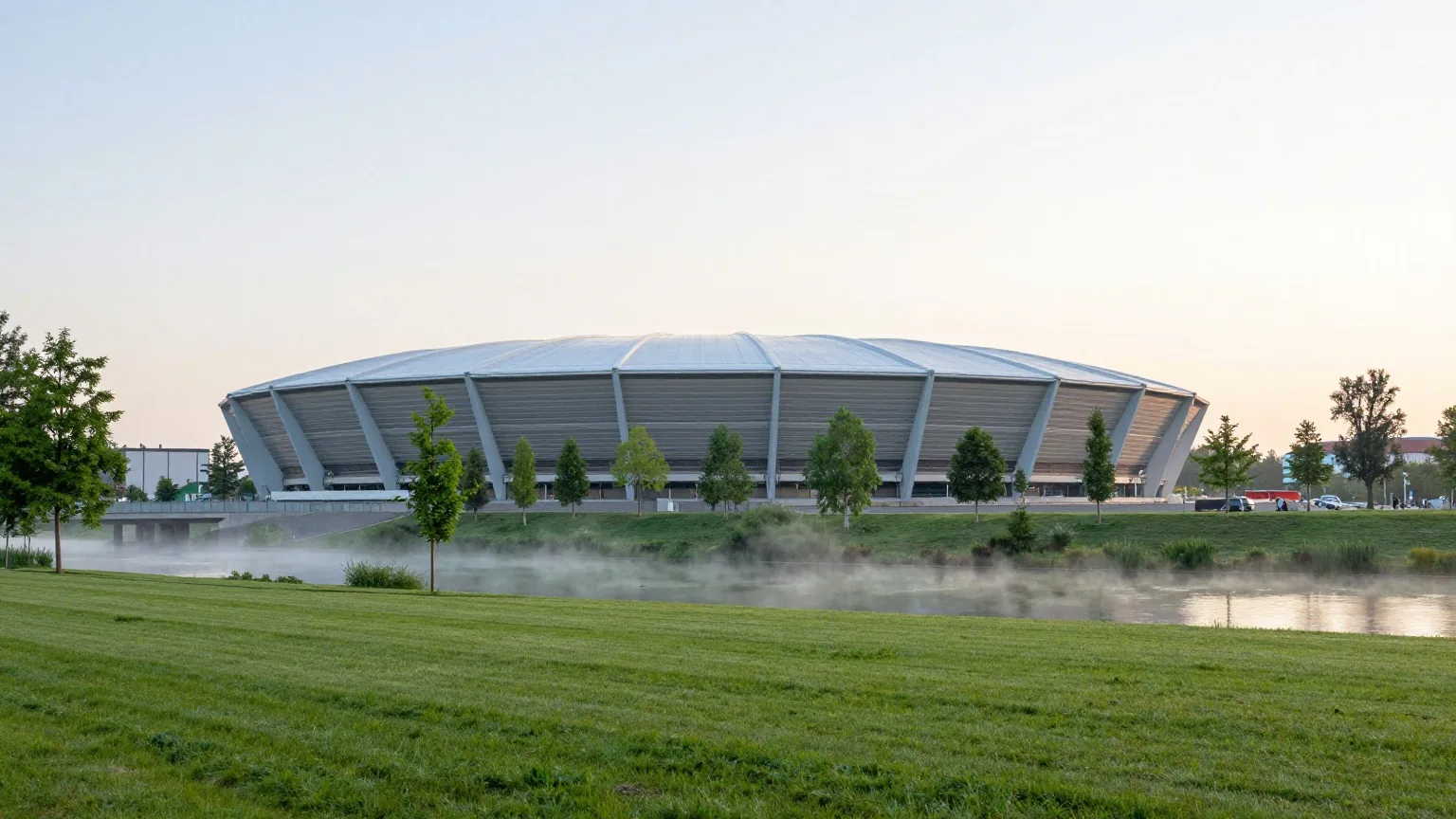 Moderne Fußballarena mit flachem lichtdurchlässigem Dach an einem Flusspark im Morgennebel mit grünen Wiesen