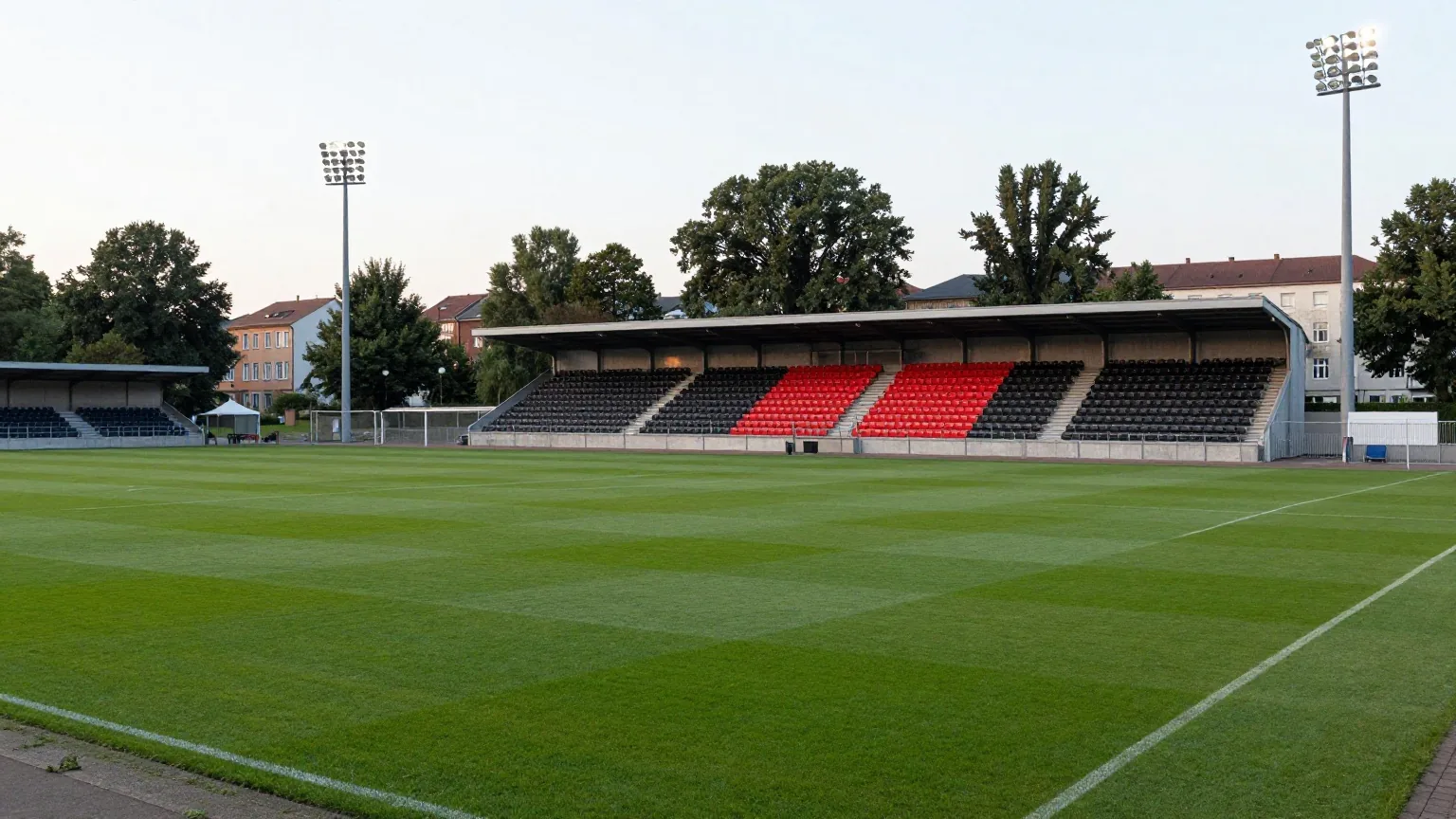 Kompaktes Fußballstadion in einem grünen Stadtpark am Abend mit schwarzen und roten Sitzen und Flutlicht