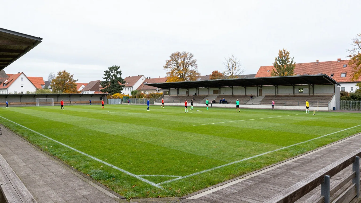 Kleines traditionelles Fußballstadion an einem grauen Herbstnachmittag mit überdachter Stehtribüne, Spieler wärmen sich auf